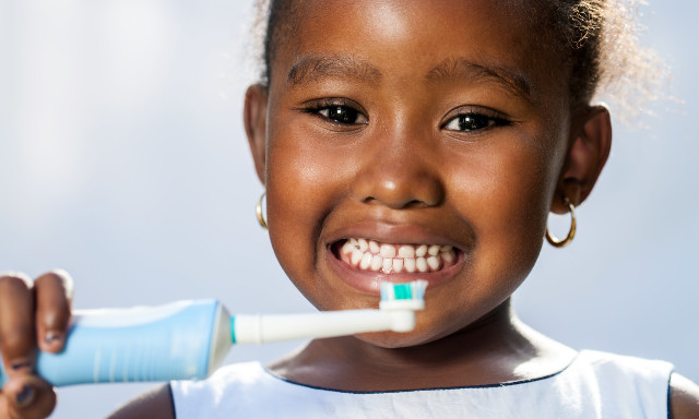 Close up portrait of cute little afro girl holding electric toothbrush ready to brush teeth.